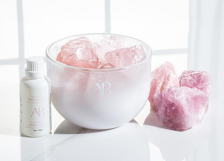 Bowl of pink bath bombs with a bottle labeled 'AR' on a white surface.