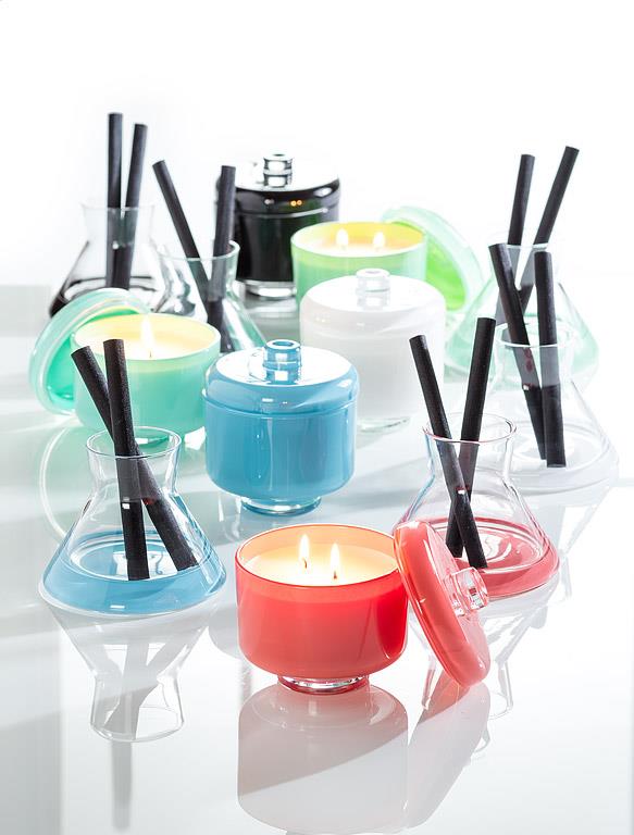 Colorful candles and containers on a reflective surface with a white background