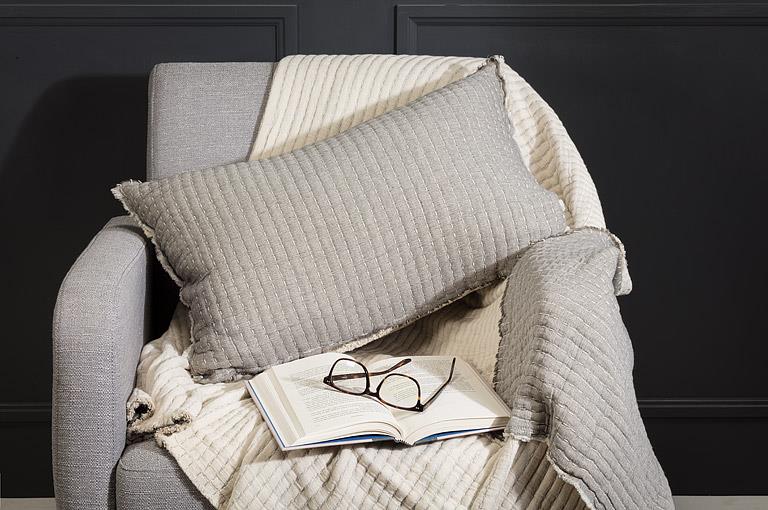 Gray textured pillow on a gray armchair with a book and glasses on a dark background