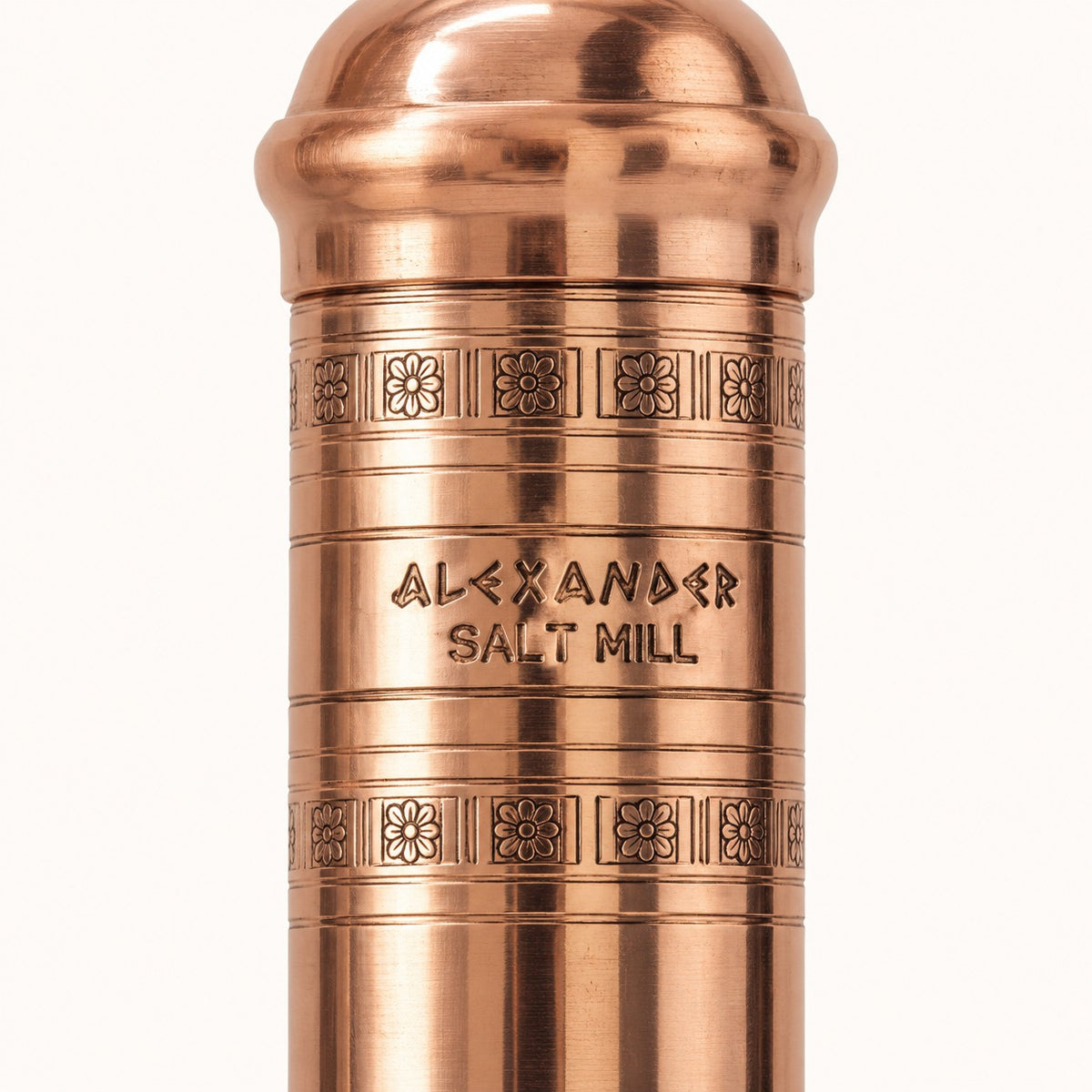 Close-up of a metallic copper-toned cylindrical container engraved with 'ALEXANDER SALT MILL' and decorative bands, shown on a plain light background.