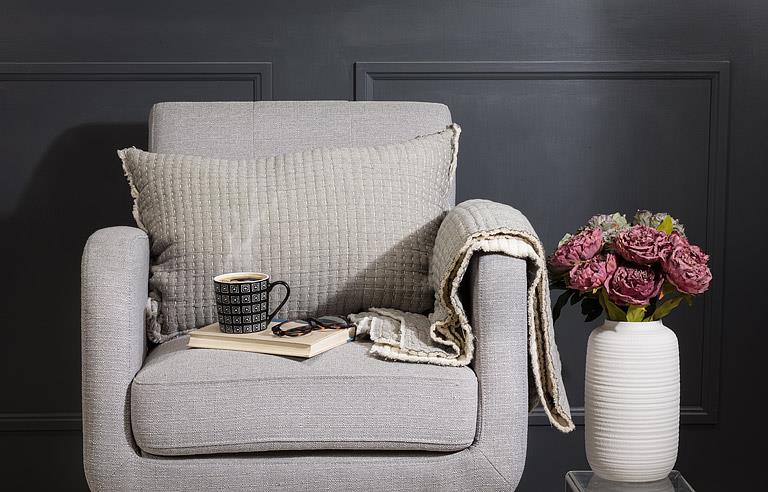 Gray armchair with a cup, book, and blanket in a room with dark walls and a vase of flowers.