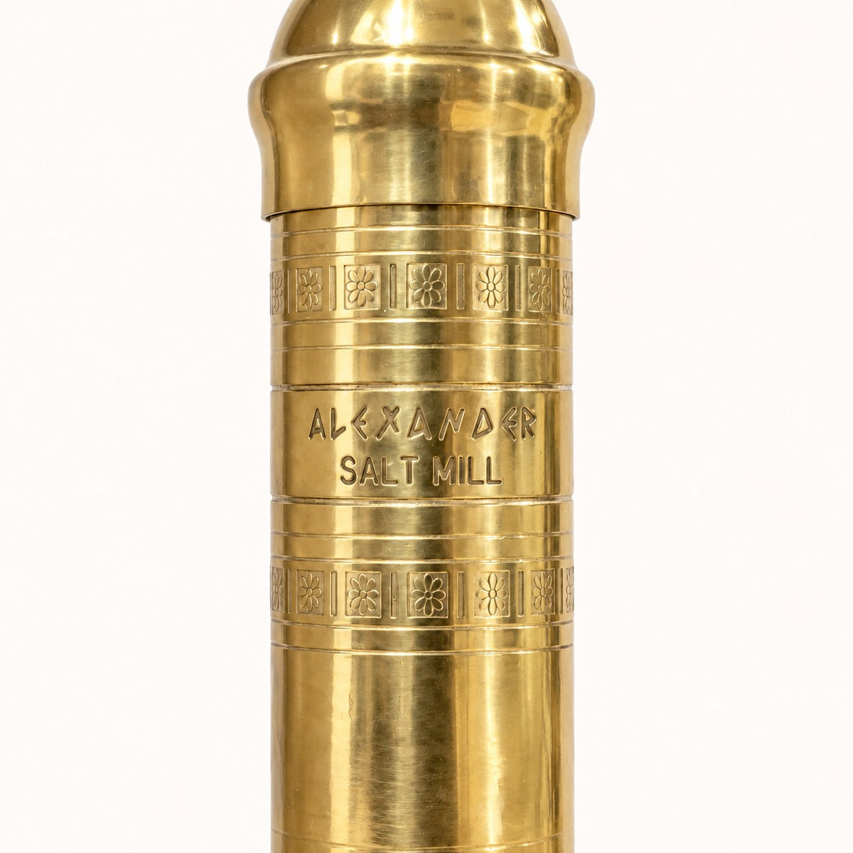 A close-up of a brass cylindrical object engraved with 'ALEXANDER SALT MILL' and decorative bands, shown against a plain white background.