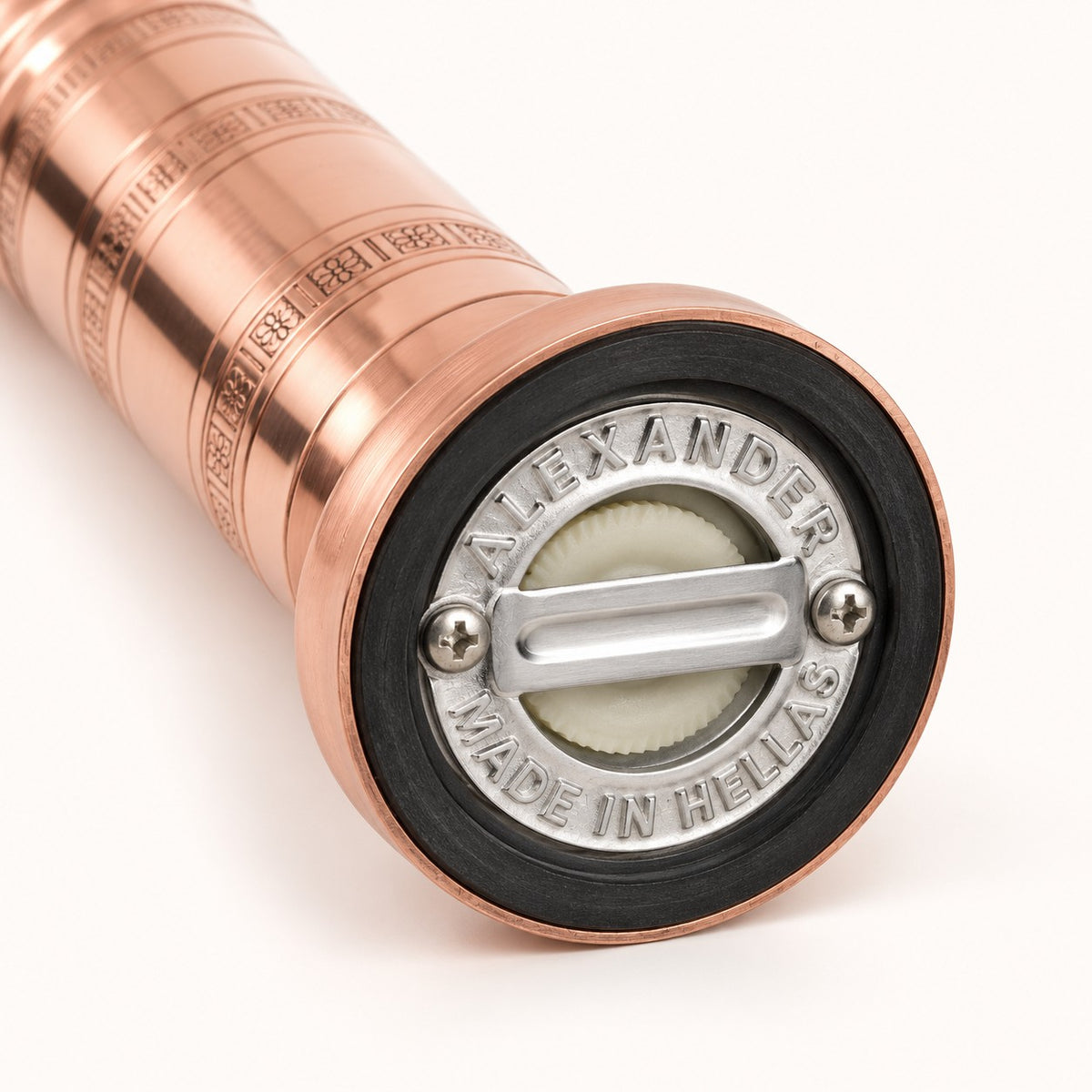 Close-up of a metallic copper-toned cylindrical object, likely a bottle or container, showing the circular end cap with a black rubber gasket, silver metal hardware, and engraved text reading 'ALEXANDER' and 'MADE IN HELLAS' on a white background.